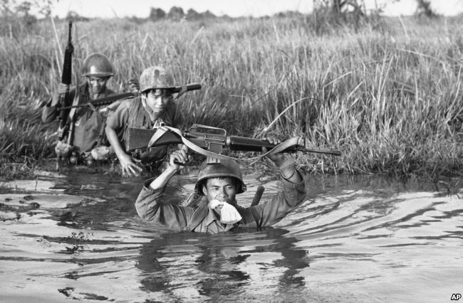 FILE - A South Vietnamese soldier holds his personal belongings in a plastic bag between his teeth as his unit crosses a muddy Mekong Delta stream in Vietnam near the Cambodian border, March 11, 1972. His unit was charged with stemming Communist infiltrat. Photo: VOA